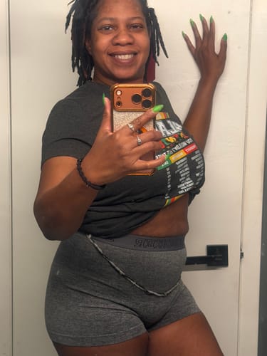 A smiling reviewer shows two combined strands of Clear Glow in the Dark Waist Beads worn over their shorts.