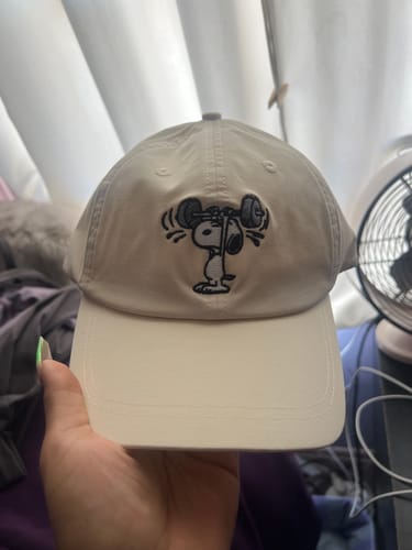 Reviewer holding their custom off-white Big Cross Training Hat with an embroidered Snoopy lifting weights.