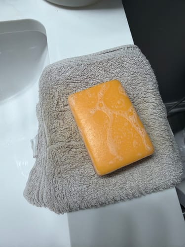 Customer's orange Turmeric Fade & Glow Bar, showing some lather, resting on a gray towel by a sink.