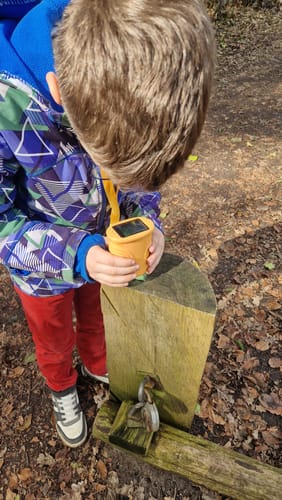 Ein Kunde untersucht mit dem orangefarbenen Edubini Abenteuer-Mikroskop einen Holzpfosten.