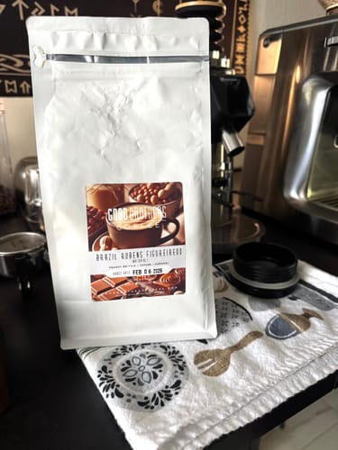 Customer's bag of Rubens Figureiredo Nogueira Natural Brazil coffee on a kitchen counter next to an espresso machine.