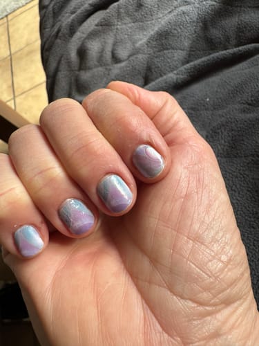 Nahaufnahme der Hand einer Kundin, die die kühlen, irisierenden „Oyster Dream“ Nagelfolien auf kurzen Nägeln trägt.