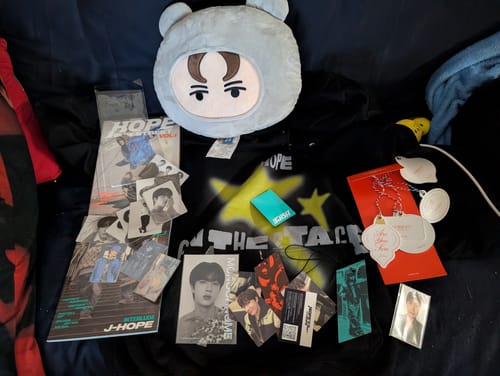 Reviewer displays the contents of their K-POP RANDOM BOX, featuring a J-Hope hoodie, plushy, and photocards.