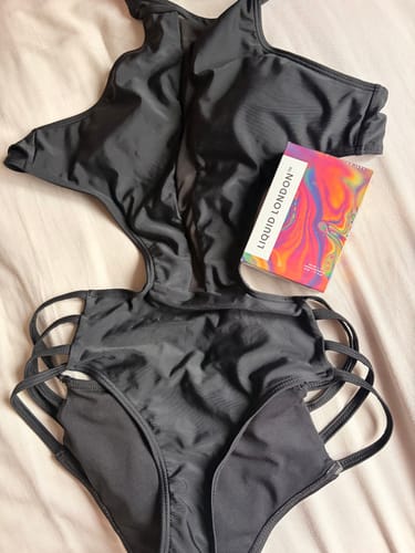 Reviewer's For Her Pheromone Perfume box resting on a black swimsuit laid out on a bed.