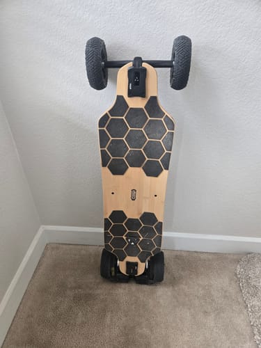 Reviewer's refurbished skateboard with large all-terrain wheels and a wood deck standing in a corner.