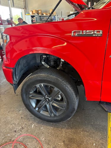 Customer's red Ford F150 on a lift, showing the installed silver Aluminum Upper Control Arm inside the wheel well.