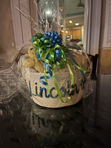Customer's personalized knitted basket with the name 'Lincoln', wrapped as a gift with a large blue and green bow.