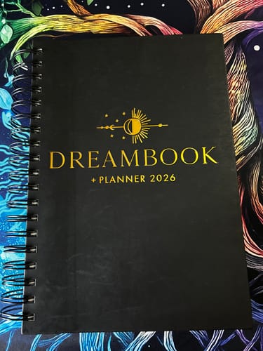 Customer's black spiral-bound 2026 Dreambook + Planner showing its gold foil cover on a colorful surface.