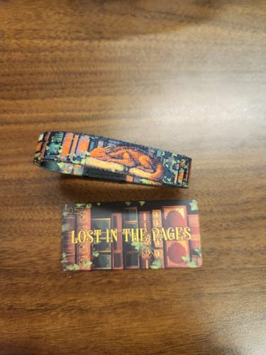 Reviewer's 'Lost In The Pages' bracelet, the Dragon version, laid out next to its matching collector's card on a wooden surface.