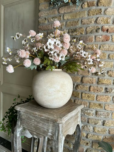 Klant toont de beige Terra vaas met een groot boeket op een houten krukje.