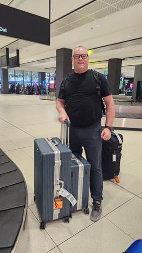 Customer with their two blue hard-shell NOBL suitcases at an airport baggage claim after a flight.