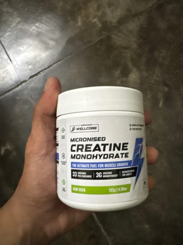 Customer holding a white tub of Wellcore Micronised Creatine Monohydrate in the Kiwi Kick flavor.