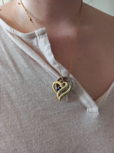 Eine Kundin trägt die goldfarbene Halskette mit vereinten Herzen und zwei blauen Geburtssteinen.
