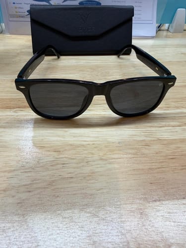 Customer's black Aurix Smart Glasses resting on a wooden table, with the black case displayed behind them.