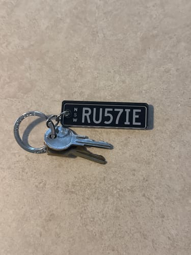 Customer's black custom licence plate keychain with 'RU57IE' text, attached to a keyring with a set of keys.