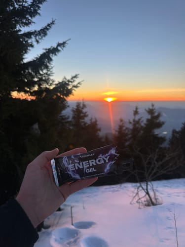 Customer holding an open Energy Gel packet in a snowy landscape with a sunrise in the background.