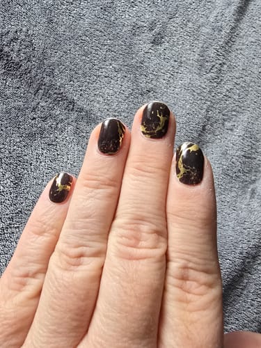 Nahaufnahme der Hand einer Rezensentin, die die Black Magic Marble UV-Gel-Folien trägt.