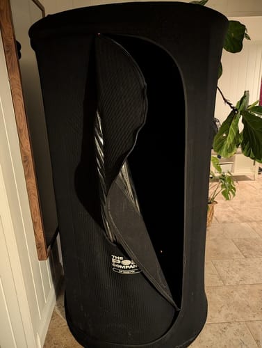 Customer's black Sauna Pod 2.0 set up indoors with the zippered door partially open.