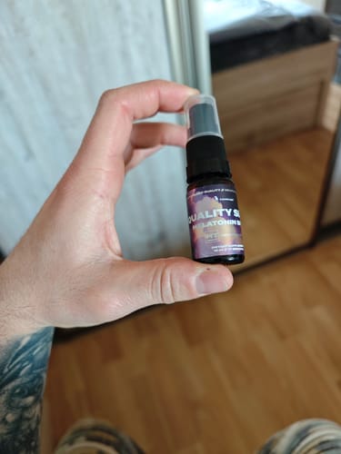 Reviewer holding the small Melatonin Sleep Spray bottle in their hand in a bedroom setting.