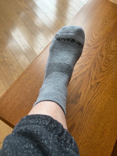 Customer wearing a grey Quarter Sock, with their foot resting on a wooden surface.