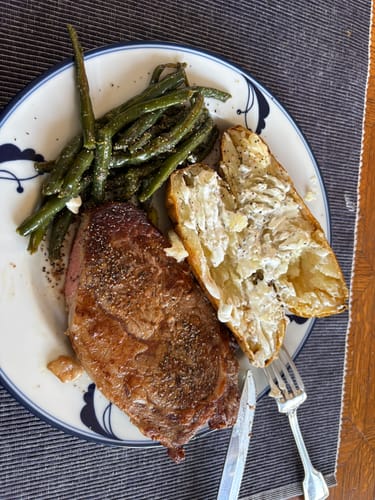 Customer's cooked Boneless Ribeye Steak plated with seasoned green beans and a baked potato.