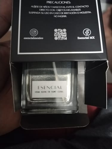 Cliente sosteniendo una caja negra abierta con un frasco de perfume Esencial adentro.