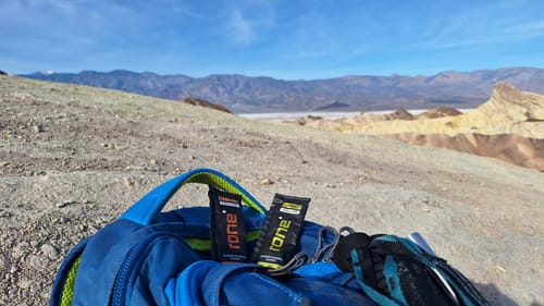 Customer's two SuperCharged Honey packets resting on a blue backpack during a hike in a desert canyon.