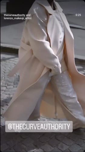 Customer walking on a cobblestone street in the oversized, light-colored Vegan Leather Trench Coat.
