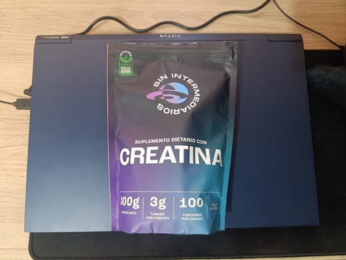 El cliente muestra la bolsa de Creatina Monohidrato sobre un portátil cerrado.