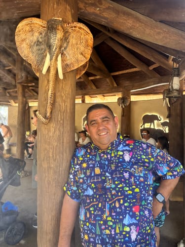 Reviewer smiling while wearing the colorful Disney's Zootopia 'Urban Jungle' shirt inside a themed lodge.