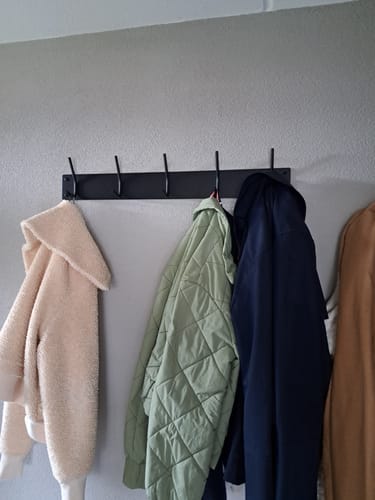 Klant toont de zwarte Spinder Design Fusion 5 wandkapstok aan een grijze muur met diverse jassen eraan.