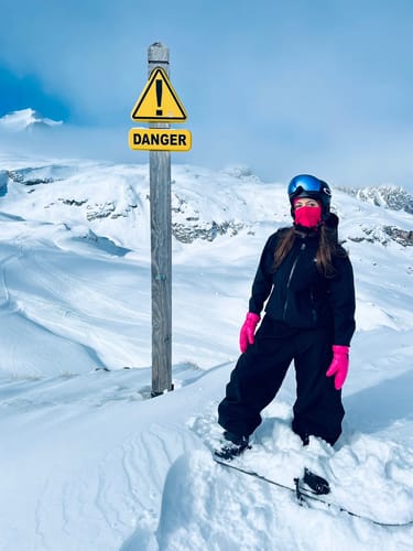 Reviewer wearing the black baggy snow pants while standing on a snowboard on a snowy mountain.