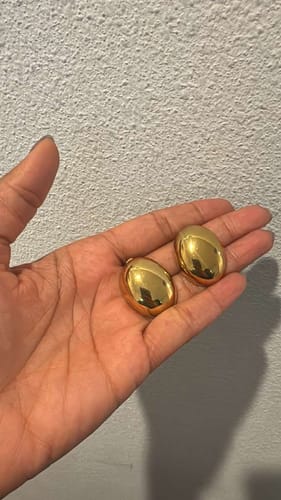 Reviewer holding the Cannes Chunky Earrings, showing their shiny, polished gold finish in their palm.