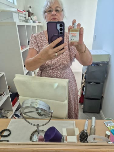 Reviewer taking a mirror selfie and holding up a bottle of Blushing Flora perfume.