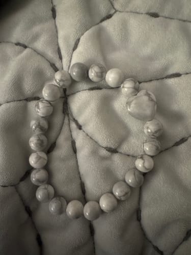 Customer's white marbled bead bracelet with a heart-shaped bead, from the Crystal Comfort package, on a quilted surface.