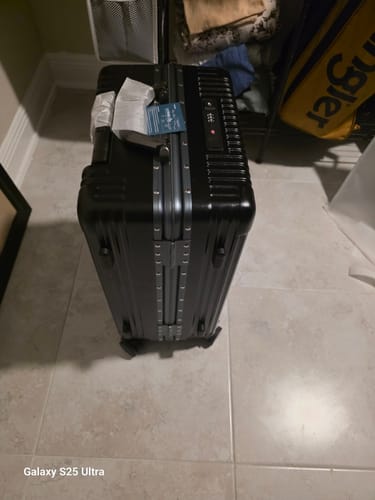 Customer's new black All-in-One Carry-On standing on a tile floor, highlighting its sturdy hard-shell exterior.