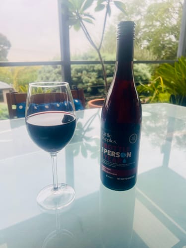 A customer's bottle of Pinot Noir sits next to a glass of the red wine on a table outdoors.