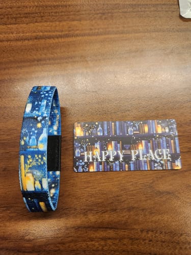 Customer's blue Happy Place Bracelet and its collector card laid out, showing the bookshelf and candle design.