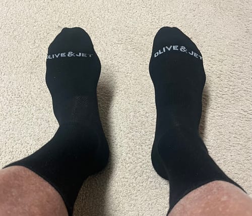A customer wearing a pair of well-fitting black Quarter Socks with the 'Olive & Jet' logo on the toes.