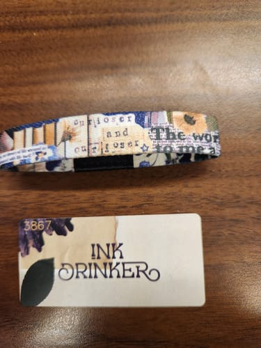 Customer's Inkdrinker Bracelet with a colorful word-collage design, shown with its matching collector's card on a wooden surface.