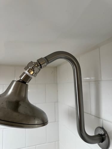 Customer's metal shower head swivel adapter installed on a curved shower arm, adjusting the angle of the shower head in a tiled shower.