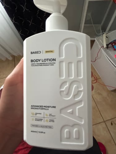 Reviewer holding the white rectangular bottle of Based Santal Body Lotion.