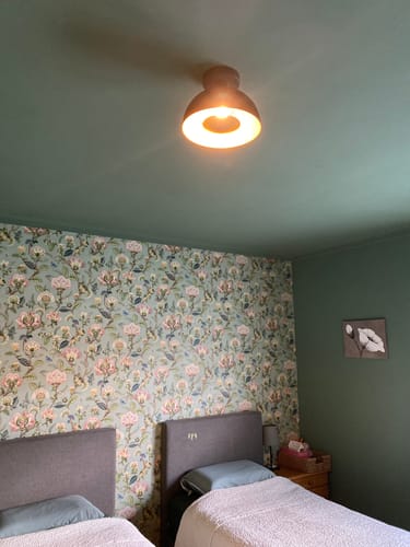 Recensent toont de groene Siemon plafondlamp, brandend aan het plafond van een slaapkamer met bloemenbehang.