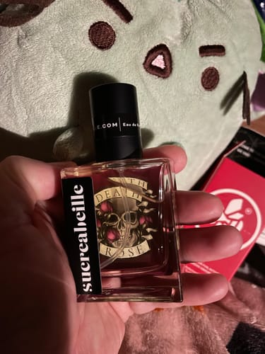 Customer holding a square glass bottle of Death Rose perfume, showing the label with a skull and roses.