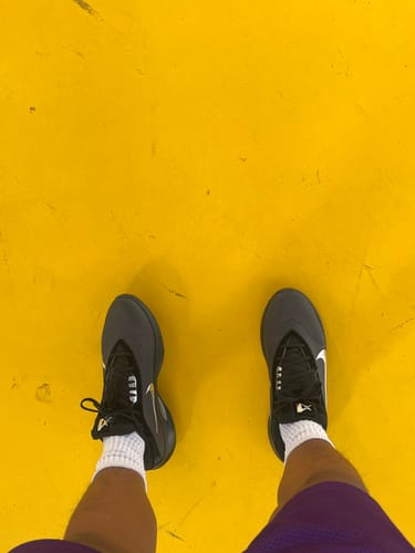Overhead view of a reviewer wearing the black Nike A'One 'MVPs' basketball shoes on a yellow court.