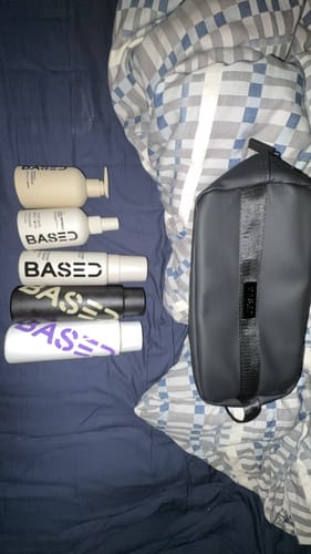 Customer's black Toiletry Bag displayed on a bed next to five product bottles.