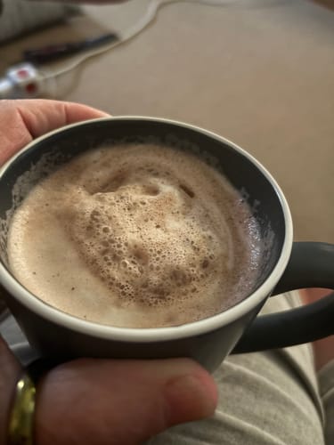 Customer holding a dark mug of the frothy Hot Chocolate PM Blend.