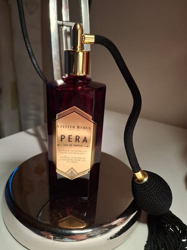 Recensent toont de Pera Eau de Parfum in een donkerrode fles met de zwarte verstuiver.