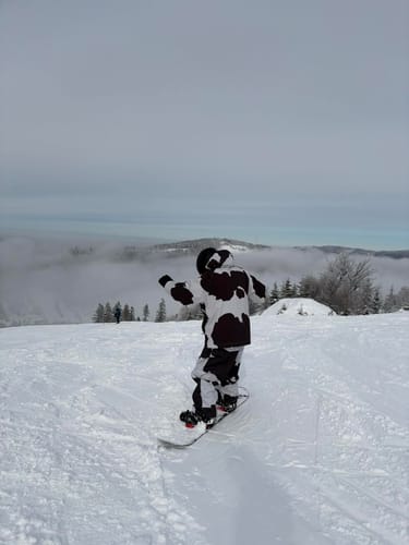 Customer wearing the Insulated Snow Jacket in a black and white pattern while snowboarding on a hill.