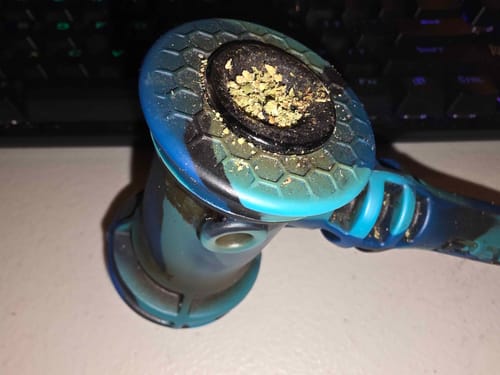 Close-up of a reviewer's blue and black pipe bowl packed with shredded Greenhouse Smalls.